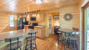 Interior de una cabaña de madera con cocina, zona de bar y una mesa de comedor con sillas.