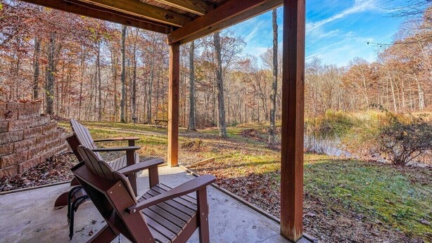 A covered outdoor seating area with wooden chairs and a view of a forested landscape.