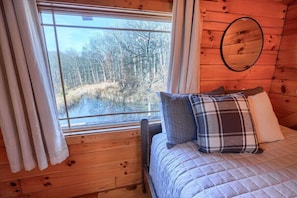 Een houten kamer met een bed, een raam met gordijnen en een spiegel aan de muur.