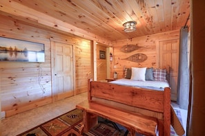 A wooden cabin bedroom with a bed, a bench, and a painting of a lake.