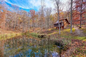 A cabin in a forest with a pond and autumn foliage.