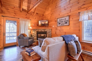 Een gezellig chalet interieur met een stenen open haard, geruite meubels en een welkomstbord.