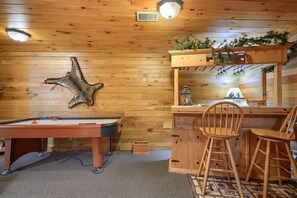 Une pièce chaleureuse avec une table de billard, des chaises en bois et un bureau agrémenté d’une plante.