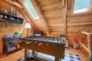 A cozy room with a wooden ceiling, a foosball table, a lamp, and a window.