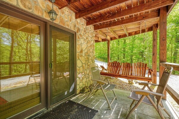 A covered outdoor seating area with stone walls and wooden beams, featuring two folding chairs and a bench.