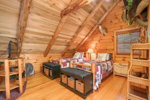 Une pièce mansardée chaleureuse avec des murs en bois, deux lits, un bureau et un ventilateur.