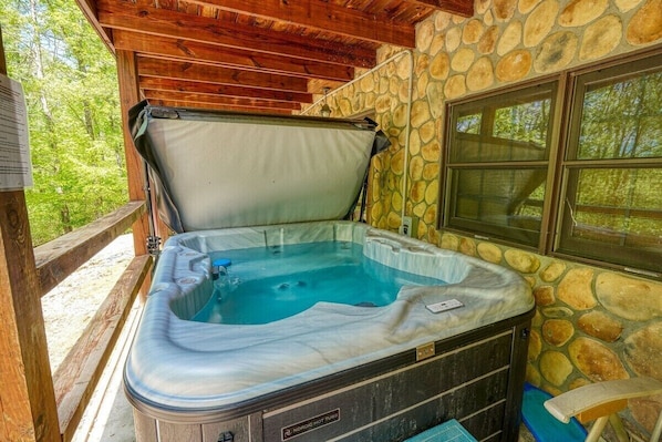 A hot tub with a stone wall and wooden ceiling, surrounded by a wooden deck.