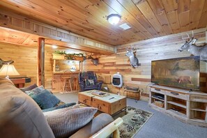 A cozy log cabin interior with a wooden ceiling, a television, a sofa, and a dining area with a chair and table.