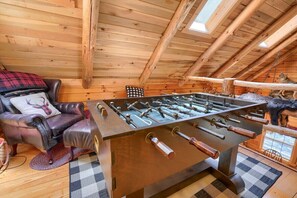 Ein gemütliches Zimmer mit Holzbalkendecke, einem Ledersofa mit kariertem Kissen und einem Kicker.