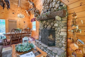 A cozy cabin interior with a stone fireplace, wooden walls, and a dining area with a table and chairs.