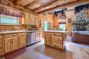 A rustic wooden cabin interior with a kitchen featuring wooden cabinets, a stone fireplace, and a dining area.