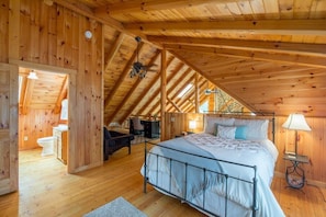 A wooden cabin bedroom with a sloped ceiling, a bed, a nightstand, and a desk.