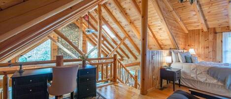 A wooden cabin with a loft bedroom, a desk, and a chair.