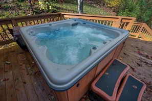 A hot tub on a wooden deck with a wooden railing and steps leading up to it.