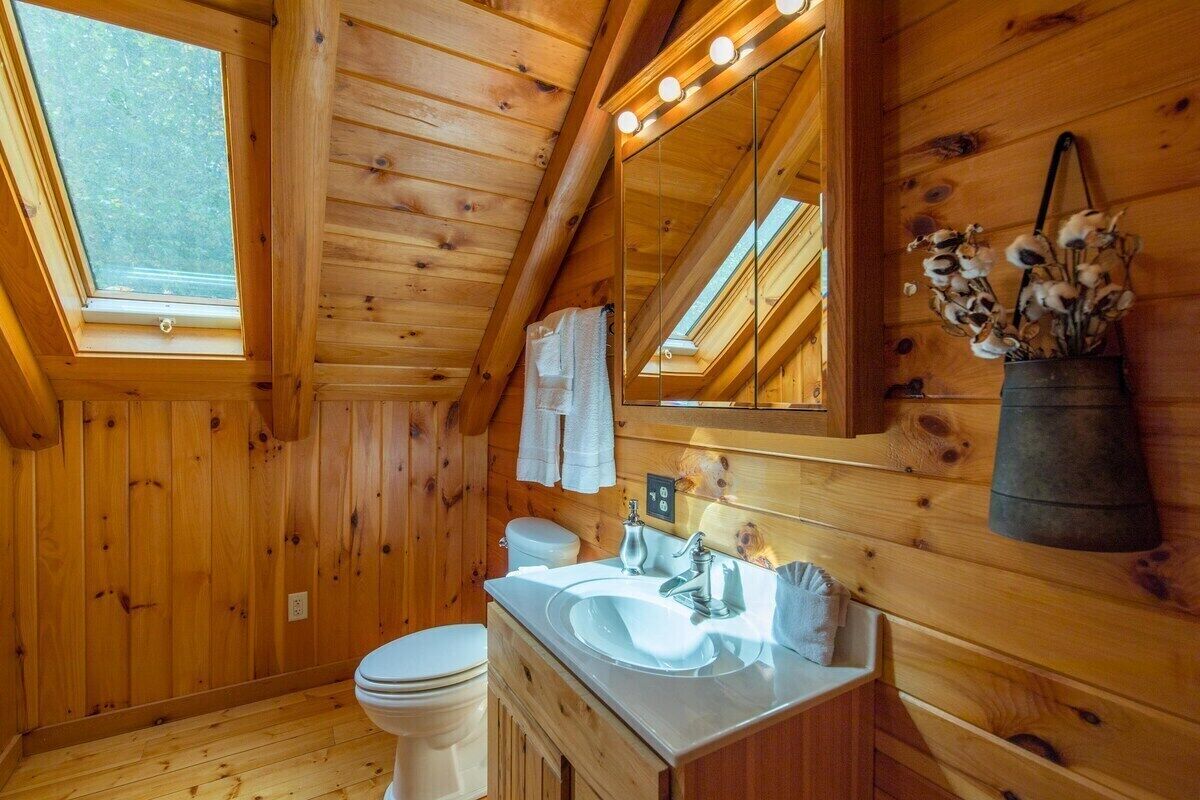 A wooden cabin bathroom with a skylight, a sink, a toilet, and a mirror.