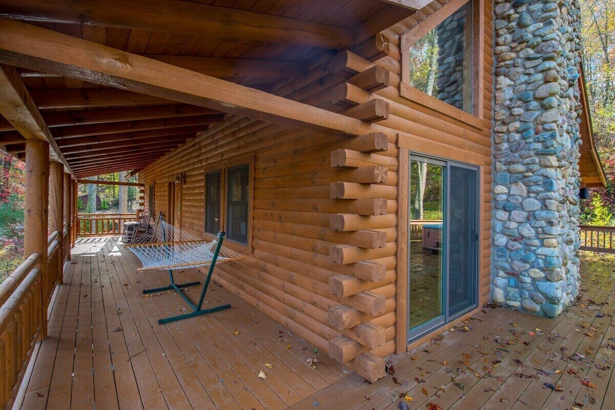 Eine Holzblockhütte mit einer Holzdielen-Terrasse, einer Steinmauer und einer Hängematte.