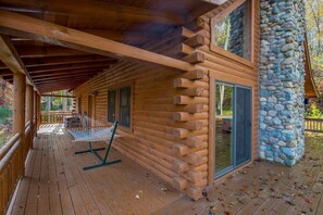 Eine Holzblockhütte mit einer Holzdielen-Terrasse, einer Steinmauer und einer Hängematte.