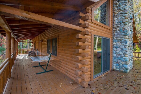 A log cabin with a wooden deck, stone wall, and a hammock.
