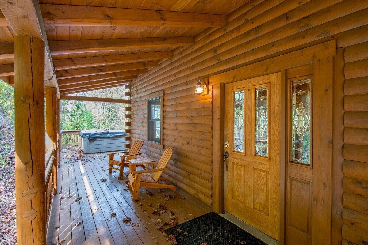 A log cabin with a wooden porch, two rocking chairs, and a covered entrance.
