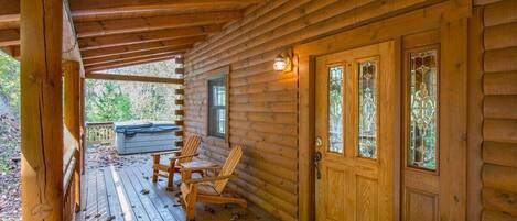 A log cabin with a wooden porch, two rocking chairs, and a covered entrance.