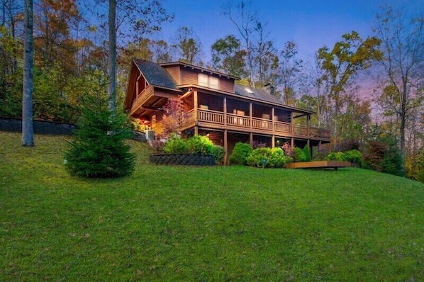 A wooden cabin with a balcony, surrounded by a well-maintained lawn and trees.