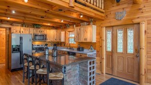 A log cabin kitchen with a central island, wooden cabinets, and a stone accent wall.