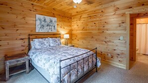 A wooden-paneled bedroom with a bed, bedside table, and a ceiling fan.