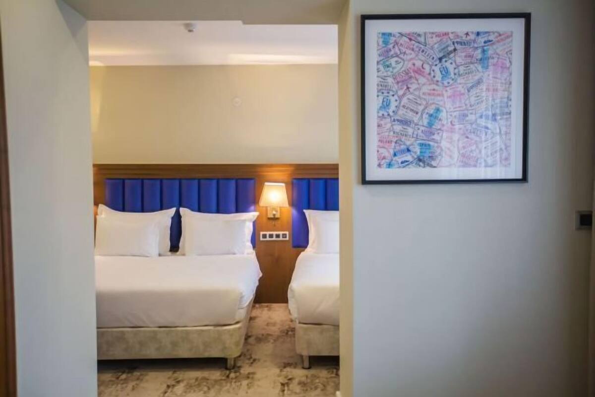 Une chambre d’hôtel avec deux lits, une tête de lit en bois, une lampe fixée au mur et une carte encadrée accrochée au mur.