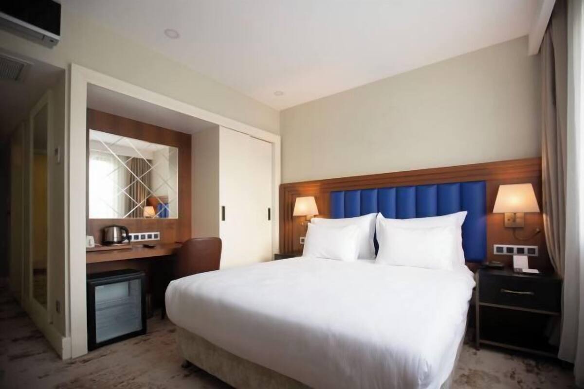 Une chambre d’hôtel avec un grand lit, des lampes de chevet, un petit bureau avec une lampe et un miroir.