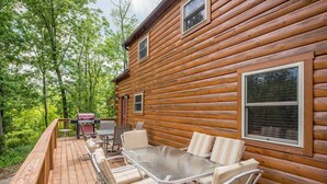 A wooden cabin with a deck, outdoor seating, and a grill.