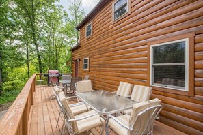 A wooden cabin with a deck, outdoor seating, and a grill.