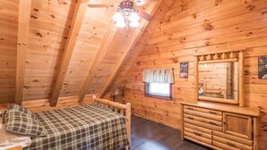 A cozy log cabin bedroom with a bed, dresser, and ceiling fan.