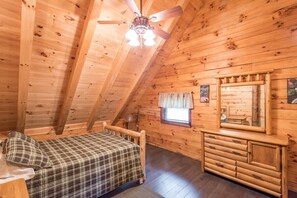 A cozy log cabin bedroom with a bed, dresser, and ceiling fan.
