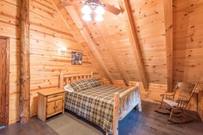 Ein gemütliches Schlafzimmer in einer Holzhütte mit einem Bett, einem Schaukelstuhl und einem Deckenventilator.