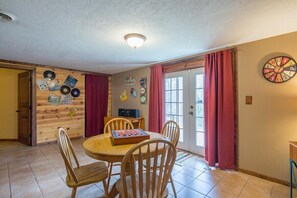 A dining area with a wooden table and chairs, a clock on the wall, and a door with red curtains.