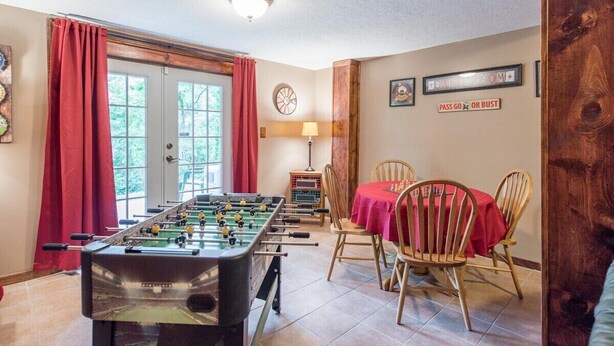 A room with a foosball table, a dining table with chairs, a clock, and a sign that says "PASS GO OR BUST".
