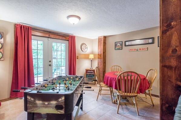 A room with a foosball table, a dining table with chairs, a clock, and a sign that says "PASS GO OR BUST".