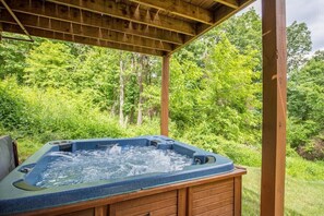 A hot tub under a wooden pergola with a forest backdrop.