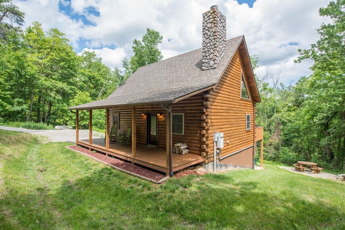 A log cabin with a porch, a chimney, and a picnic table.