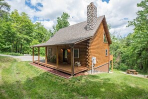 A log cabin with a porch, a chimney, and a picnic table.
