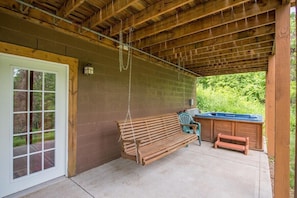 A covered patio with a wooden swing, a concrete floor, a wooden bench, and a hot tub.