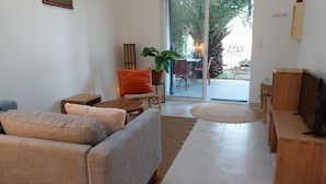 A living room with a sofa set, a coffee table, a TV, and a large window with a view of the outdoors. - Gîte La Parenthèse In a quiet Languedoc village, 8 minutes from Pézenas (Caux)