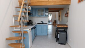 A kitchen with blue cabinets, a wooden staircase, and a dining area with a table and chairs. - Gîte La Parenthèse In a quiet Languedoc village, 8 minutes from Pézenas (Caux)