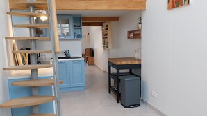 A modern kitchen with blue cabinets, a wooden staircase, and a small dining table. - Gîte La Parenthèse In a quiet Languedoc village, 8 minutes from Pézenas (Caux)