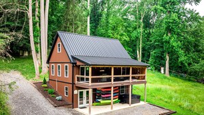 A two-story wooden cabin with a metal roof, surrounded by lush greenery.
