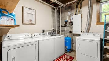Un cuarto de lavandería con cuatro lavadoras blancas, un calentador de agua azul y un letrero rojo en el suelo que indica 'Laundry Room'.