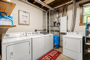 Une buanderie avec quatre machines à laver blanches, un chauffe-eau bleu et un panneau rouge indiquant « Buanderie » au sol.