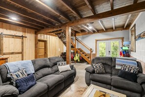 Un vaste espace de vie comprenant deux canapés, une table basse et un escalier menant à un niveau supérieur.