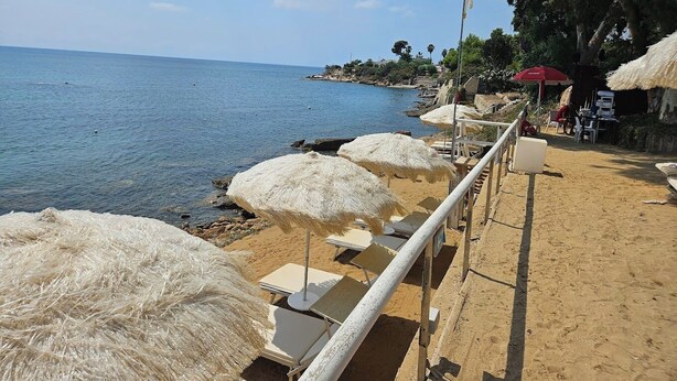 A beach with white umbrellas, sun loungers, and a railing overlooking the sea. - Cala Coralli (Syracuse)