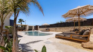A pool area with lounge chairs and umbrellas, surrounded by plants and a stone wall. - Cala Coralli (Syracuse)